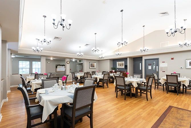An elegant dining room with neatly arranged tables and chairs, illuminated by chandeliers.