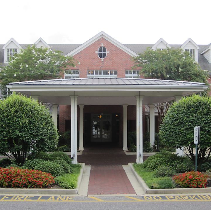 A building entrance with a covered walkway, surrounded by neatly manicured bushes and trees.