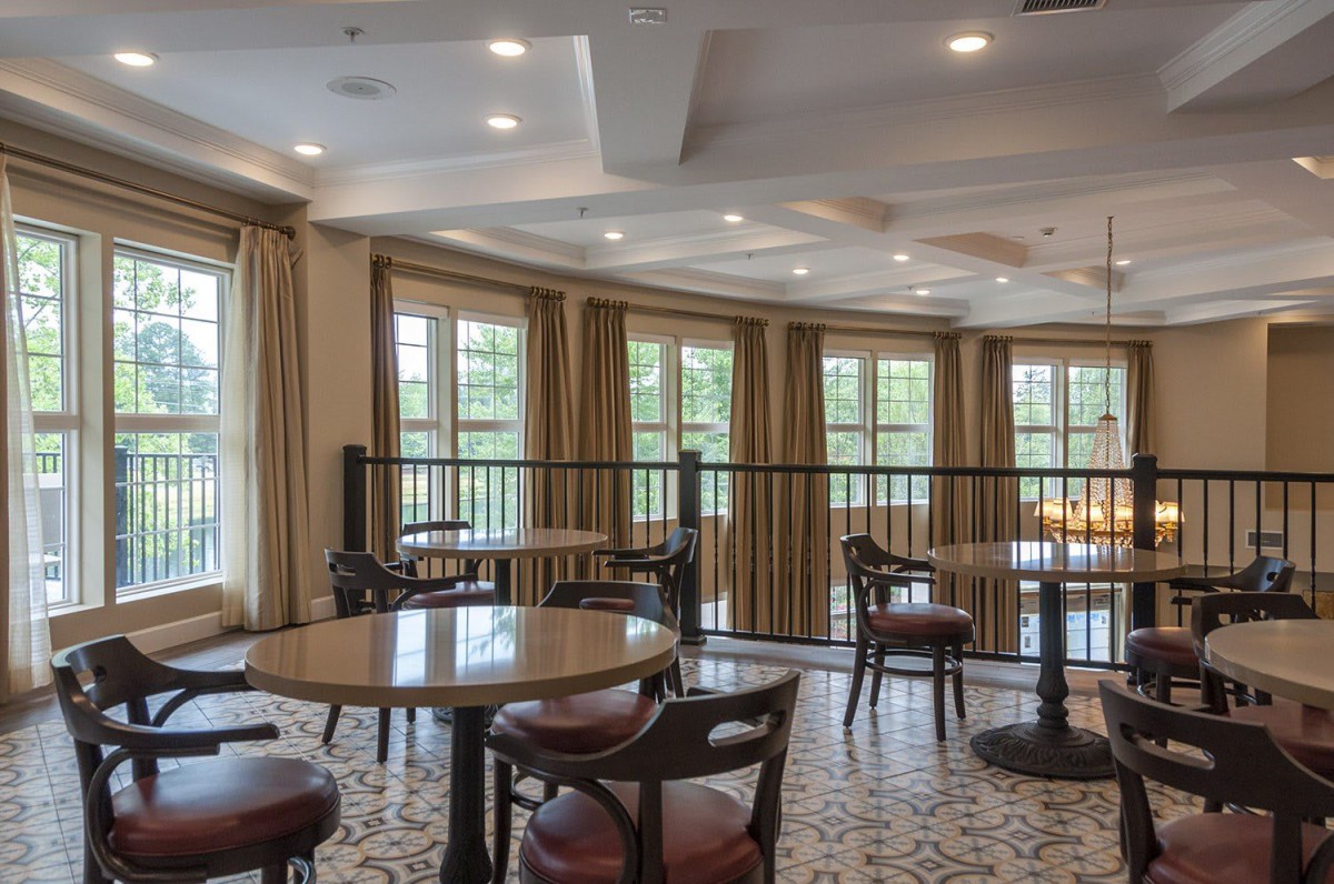 A cozy dining area with tables and chairs, illuminated by natural light from large windows.