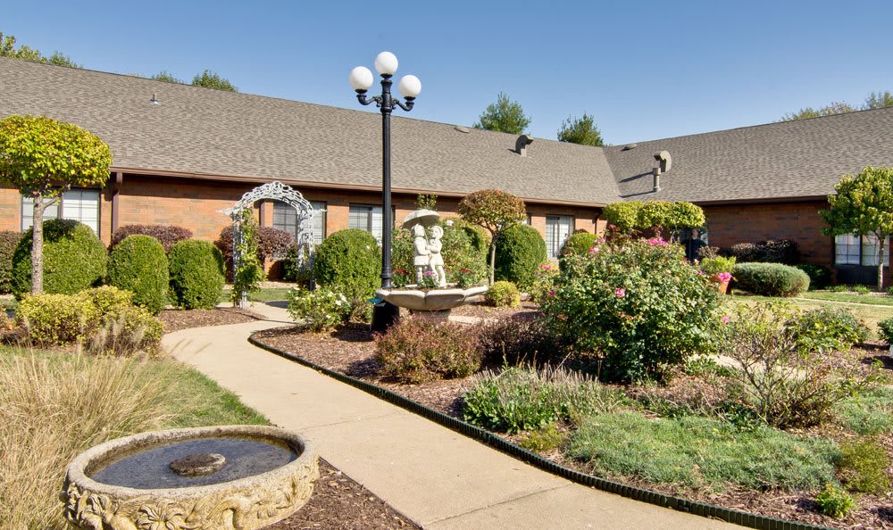 A beautifully landscaped garden featuring a stone pathway, fountains, and manicured bushes.