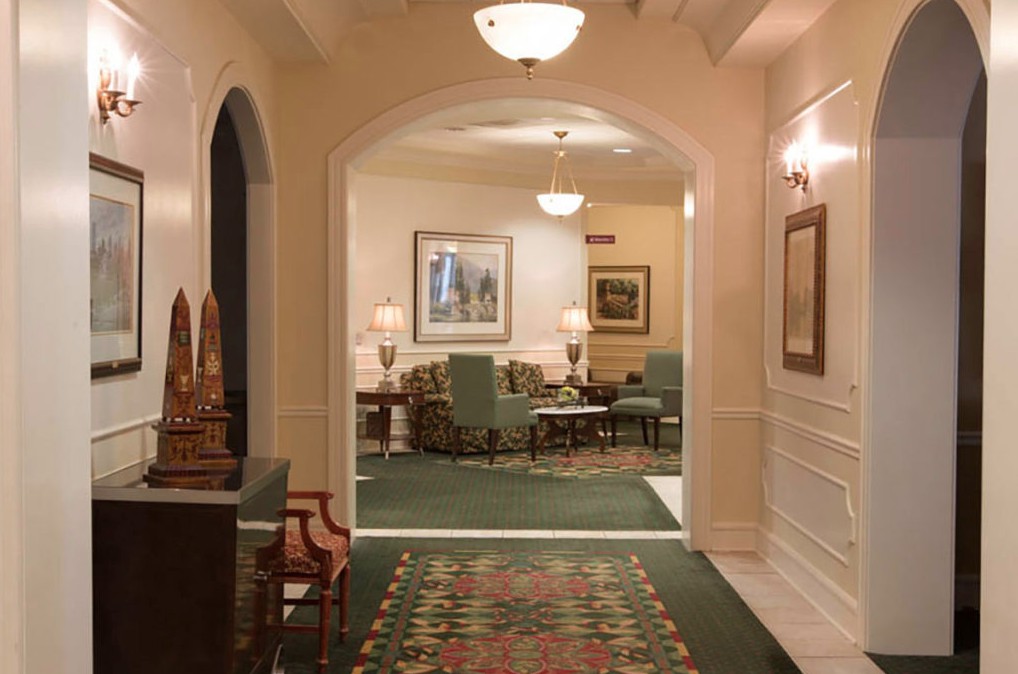 A warmly lit hallway leads into a traditionally decorated sitting area with green carpet and classic furniture.