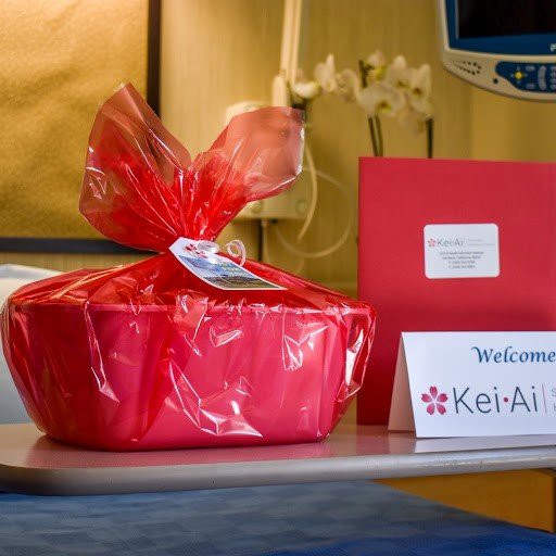 A red gift basket and welcome card placed on a table in a hospital room.