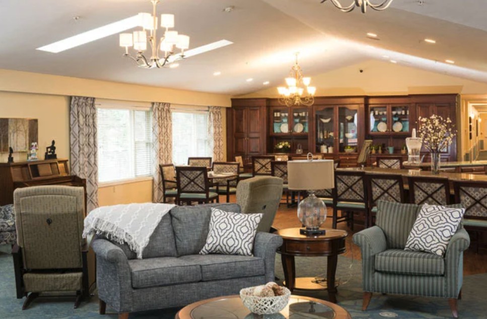 A cozy living room with sofas and a dining area in the background, featuring elegant chandeliers and warm lighting.