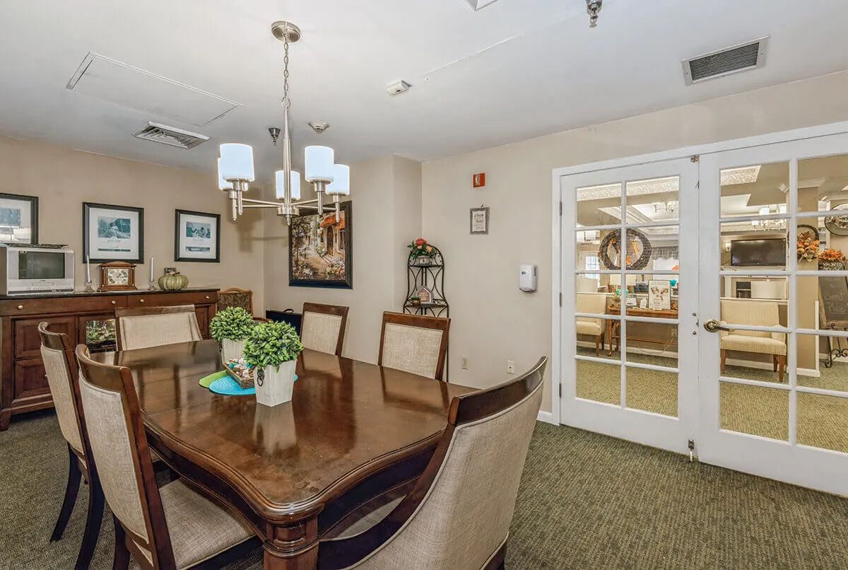 A cozy dining room with elegant furniture and decor, featuring a wooden table, upholstered chairs, a chandelier, and decorative plants.
