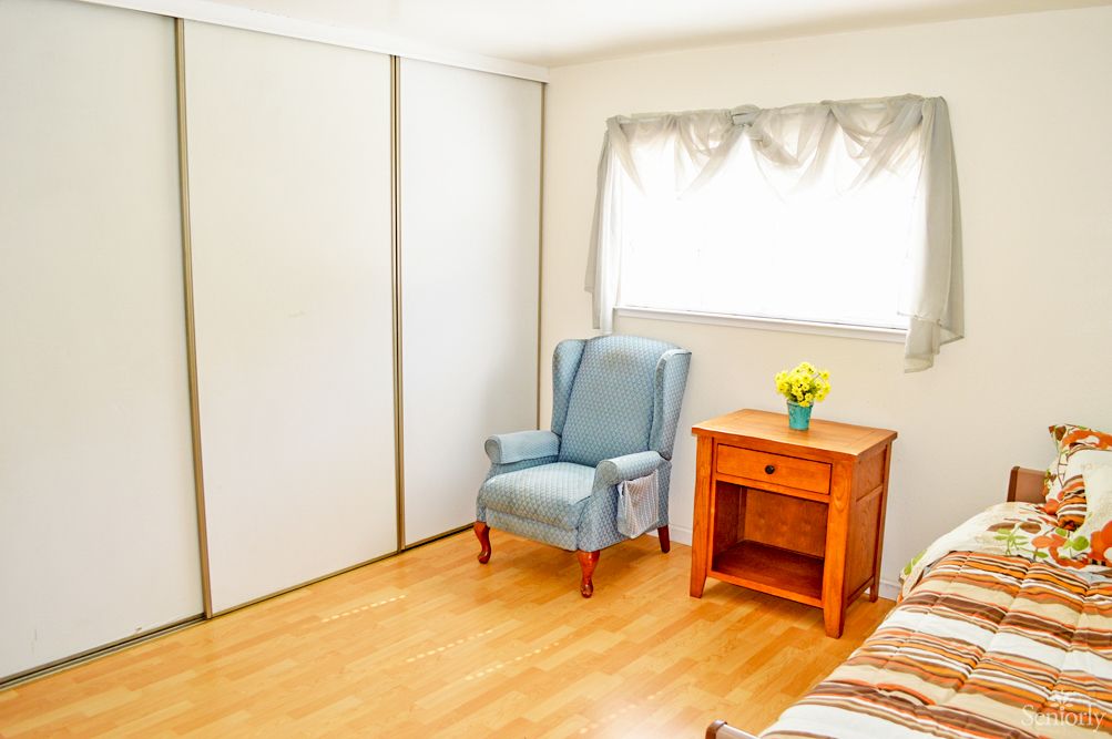 A minimalist bedroom with a blue armchair and wooden nightstand beside a window.