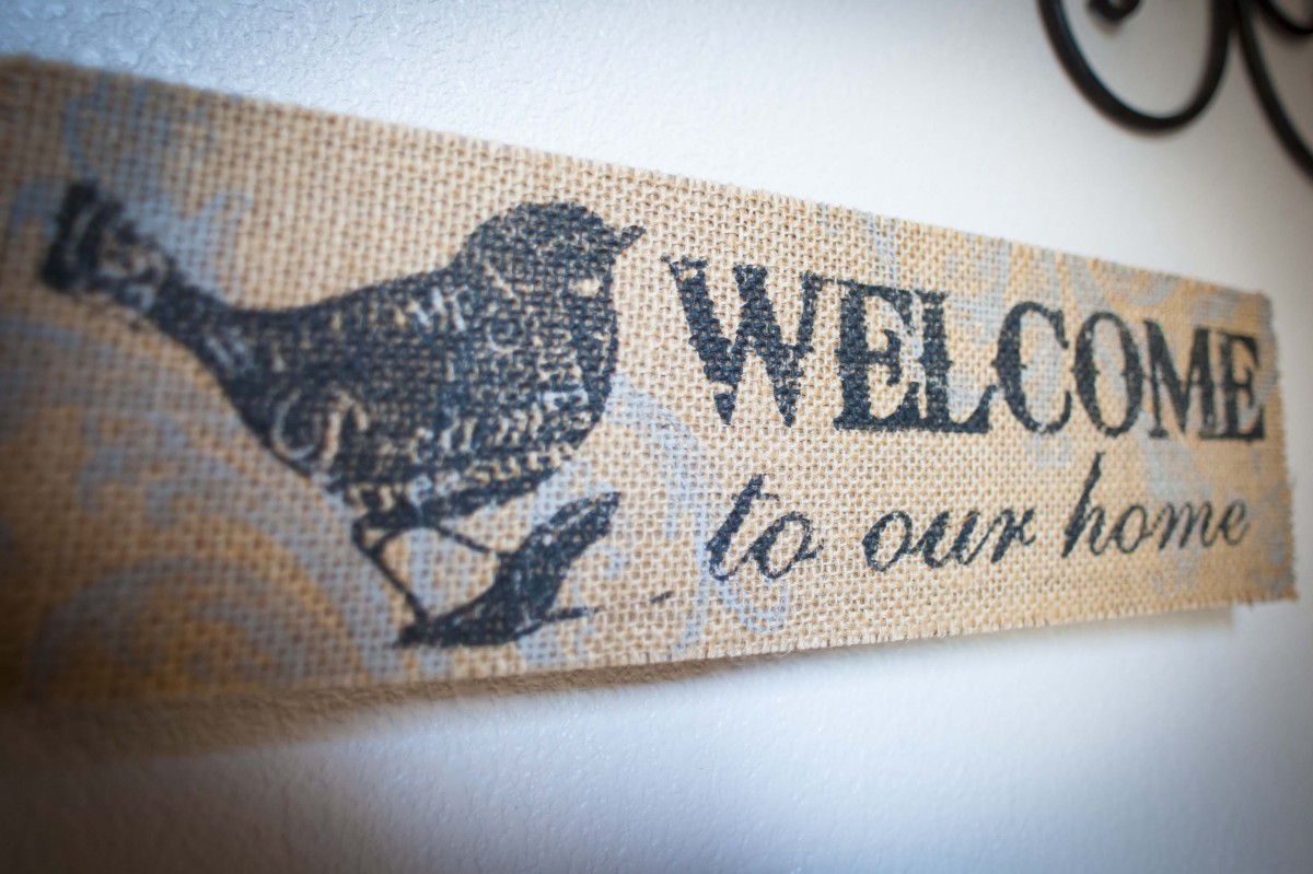 A rustic welcome sign with a bird design on fabric.