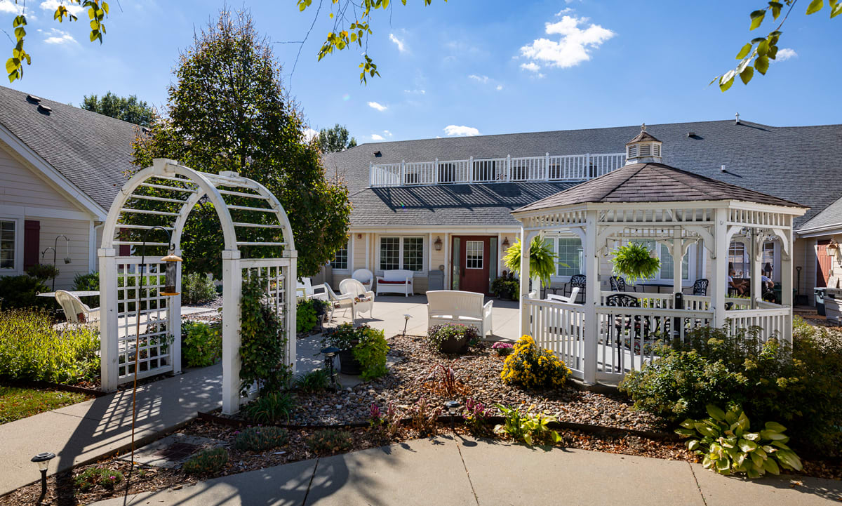 A beautifully landscaped outdoor area featuring a gazebo and archway under a sunny sky.