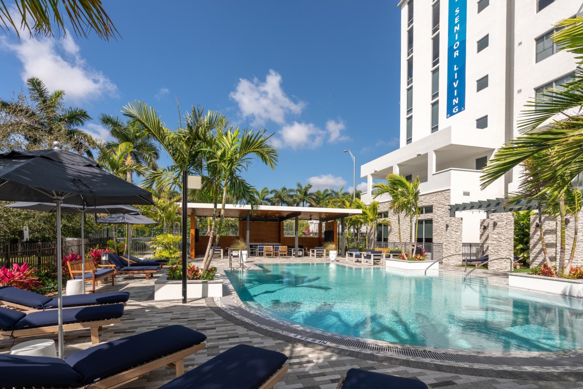A modern hotel pool area with palm trees and lounge chairs under a clear blue sky.