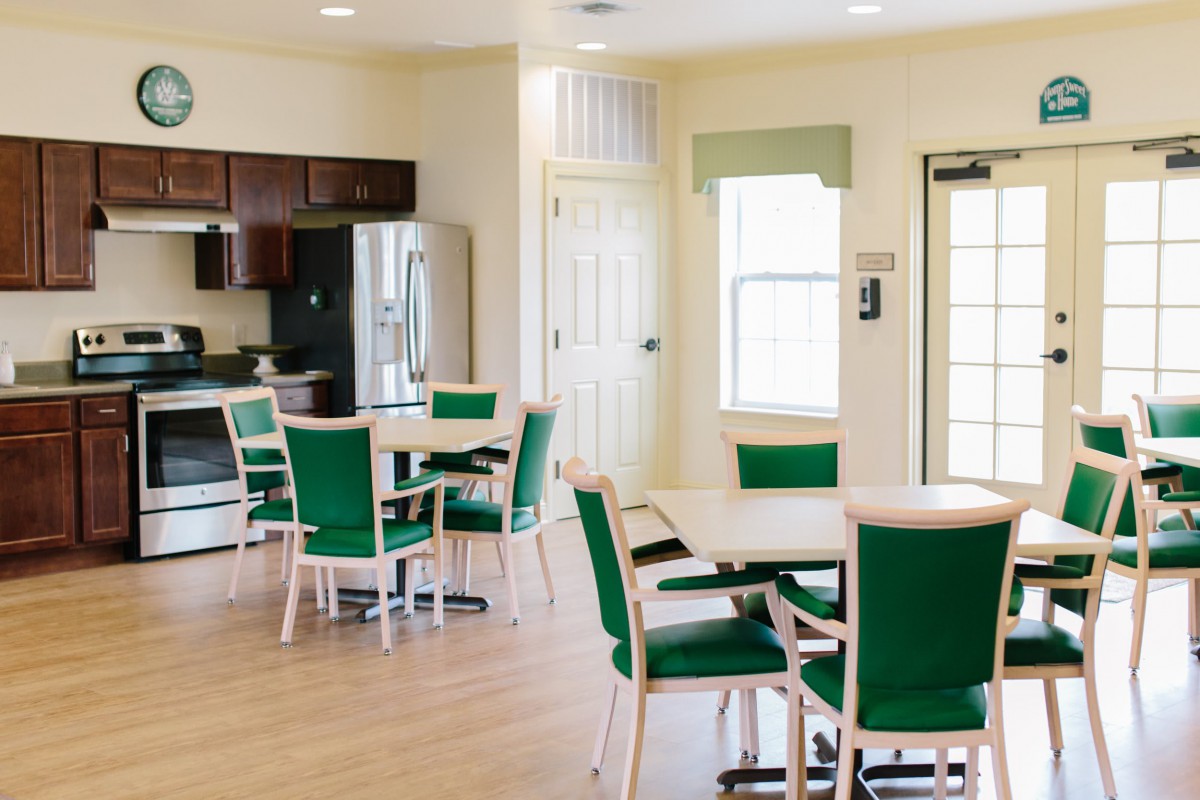 A modern dining area with green chairs and tables, adjacent to a kitchen with stainless steel appliances.