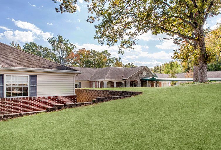 A peaceful residential building surrounded by a well-maintained lawn and trees under a partly cloudy sky.