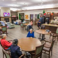 A cozy indoor community space in a senior living facility, featuring elderly residents seated around tables.