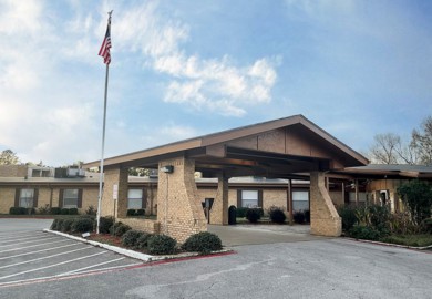A single-story building with a covered entrance and an American flag in the parking lot.