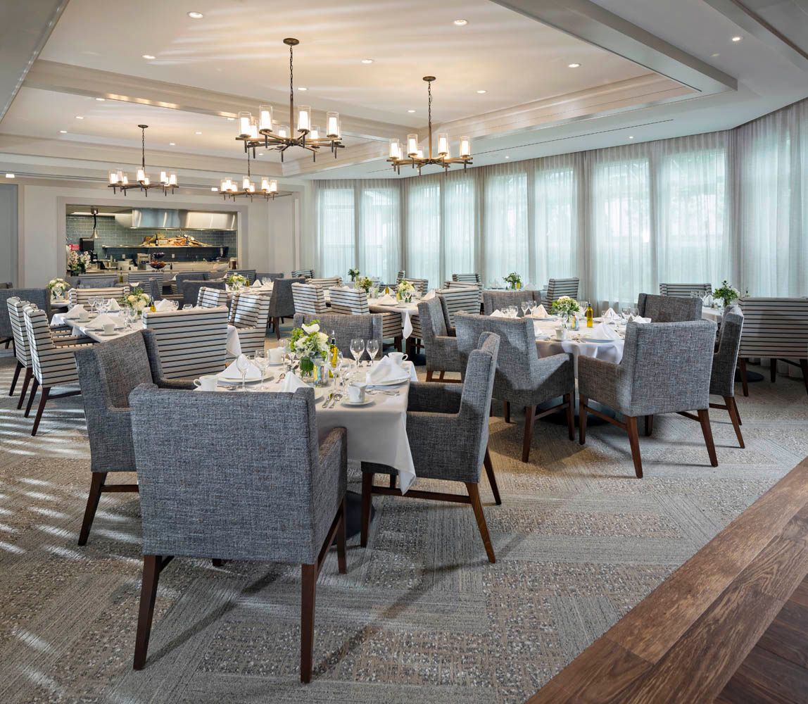 An elegantly set dining room with neatly arranged tables and comfortable chairs, featuring stylish chandeliers and decor.