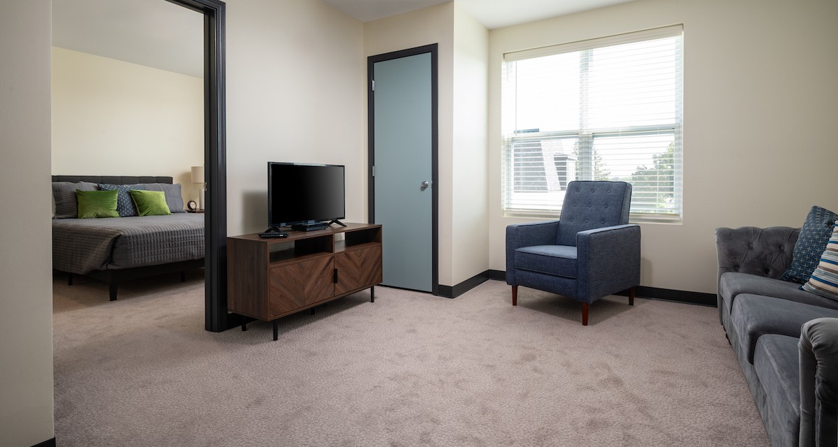 A cozy living room with a television, armchair, and large window.