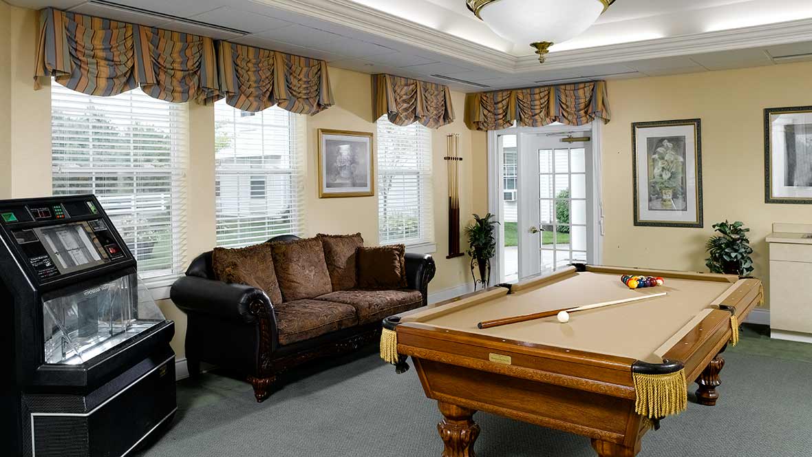 A cozy living room with a pool table and a comfortable couch, featuring large windows that let in natural light.