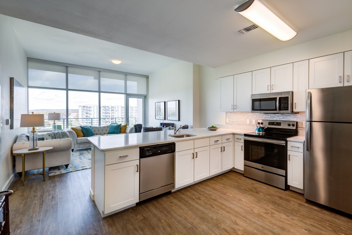 A modern kitchen with white cabinets and stainless steel appliances, featuring an open floor plan and a central island.