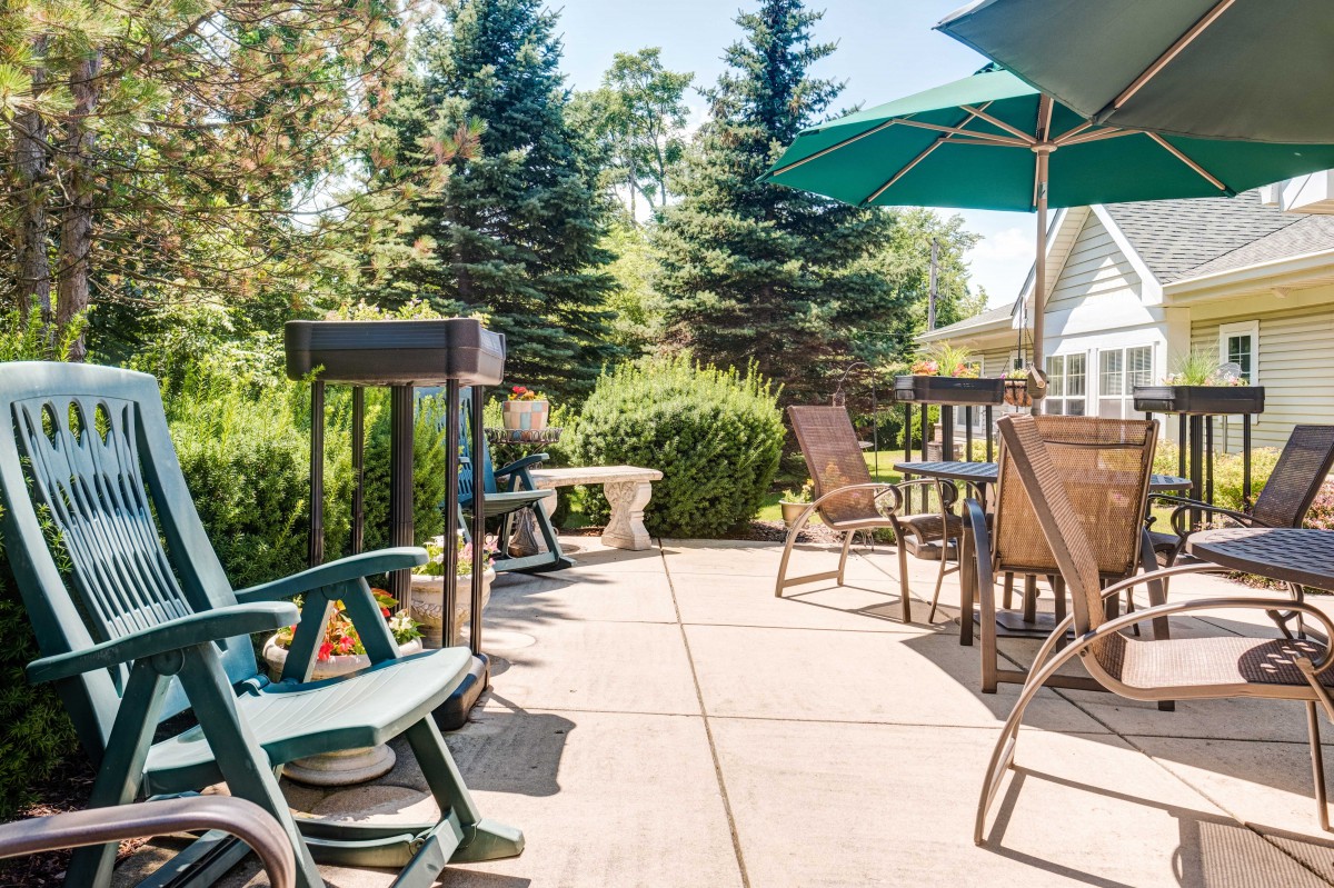 A sunny patio with outdoor seating and umbrellas surrounded by lush greenery.