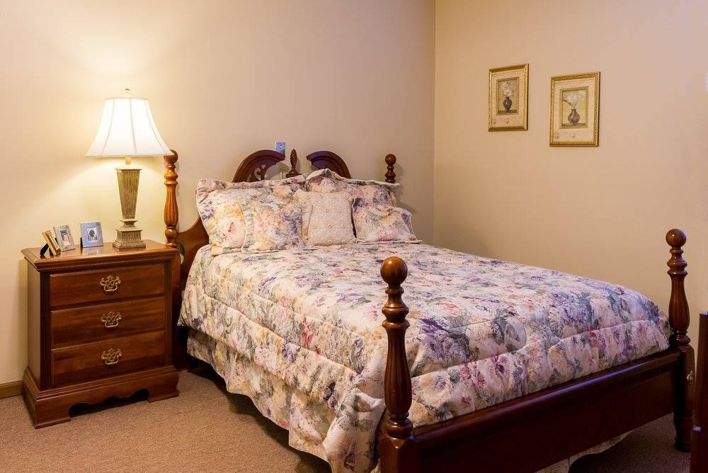 A cozy bedroom with a floral-patterned bedspread and a bedside lamp.