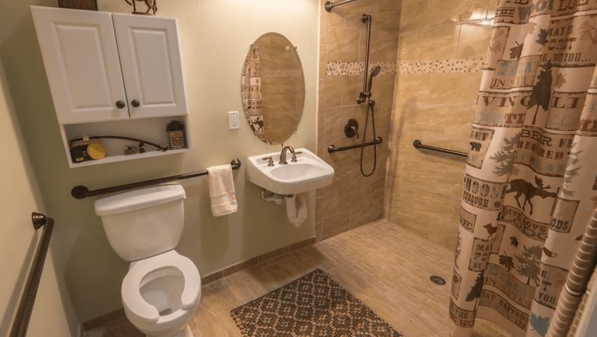 A modern, accessible bathroom with a sink, toilet, open shower, and grab bars.