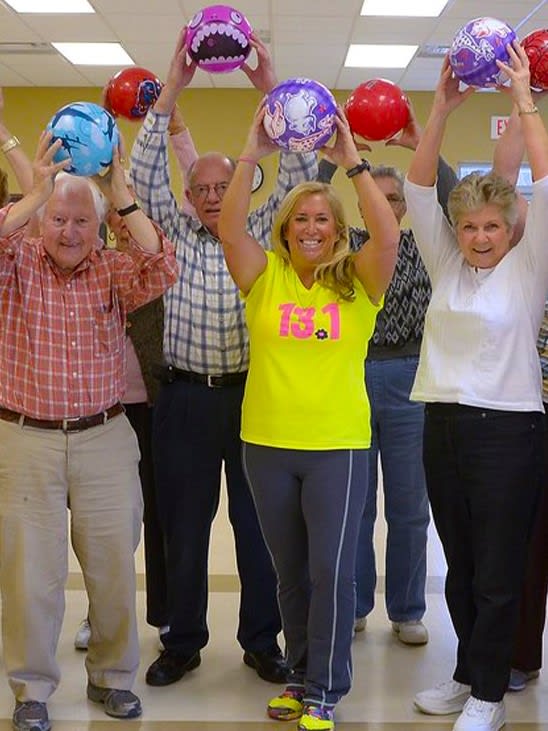 A group of people holding bowling balls over their heads and smiling indoors.