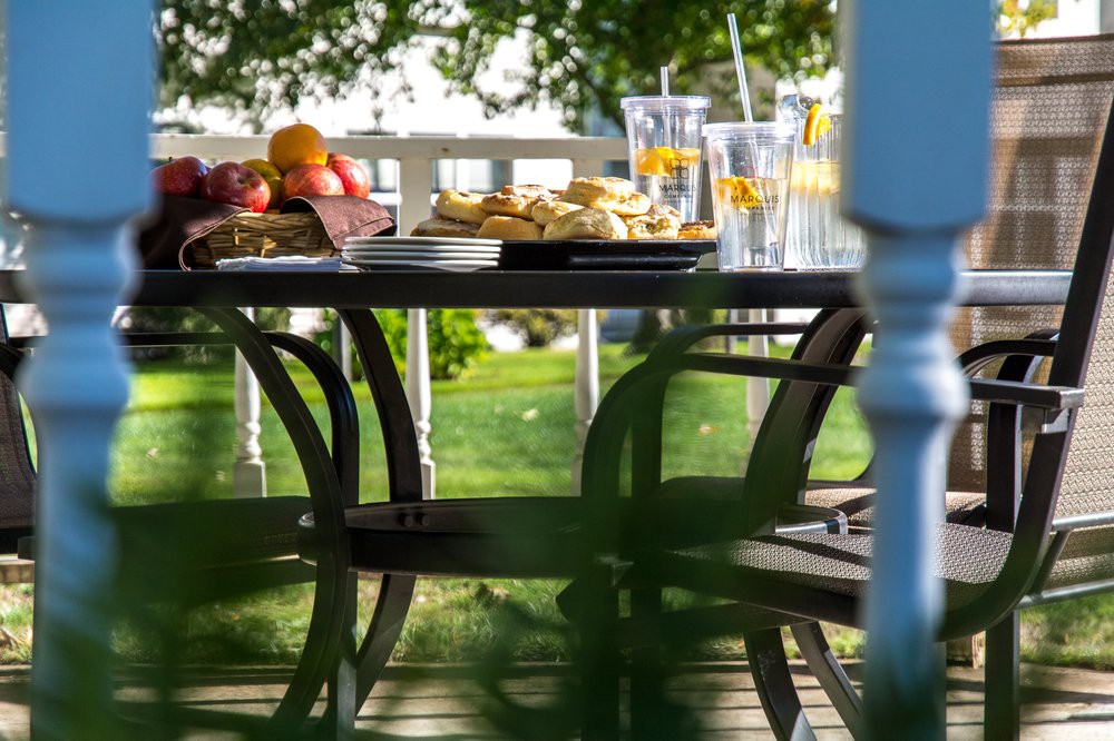 An inviting outdoor table set with food and drinks, surrounded by a lush garden.