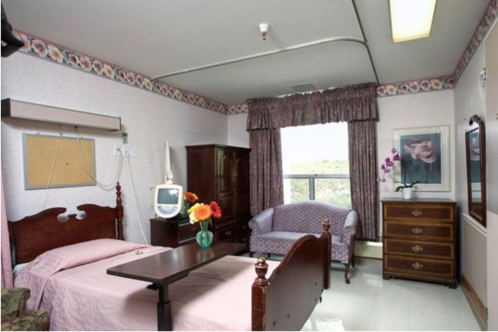 A hospital room with a patient bed, television, and furniture.