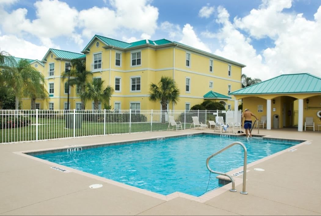 A hotel with a sunny outdoor swimming pool surrounded by palm trees.
