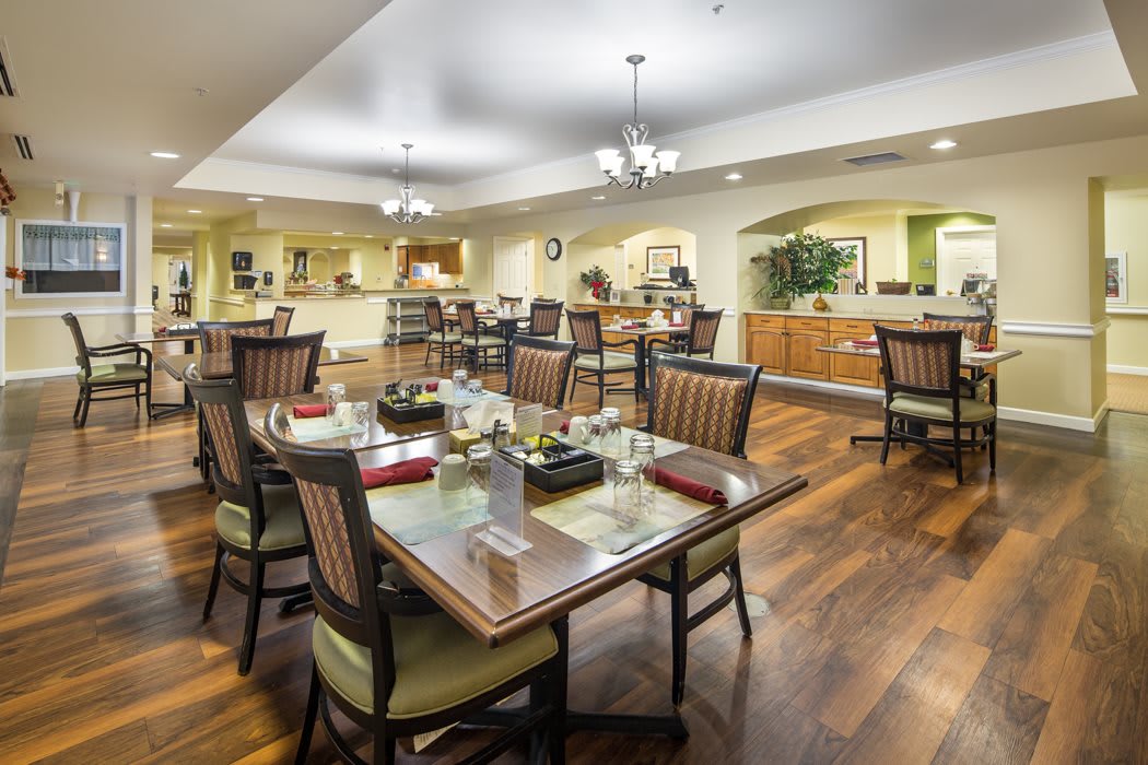 A well-lit dining area with neatly arranged tables and chairs, featuring wooden flooring and elegant lighting fixtures.