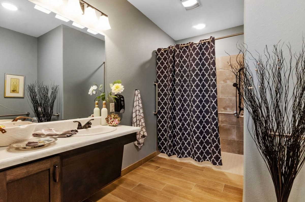 A modern bathroom with wooden flooring, featuring a stylish sink area and patterned shower curtain.