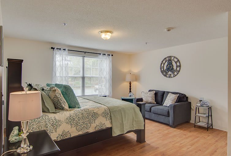 A cozy bedroom with a large bed, sofa, and natural lighting from a window.