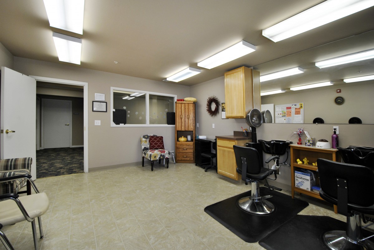 An empty barbershop interior with a barber chair and bright overhead lighting.