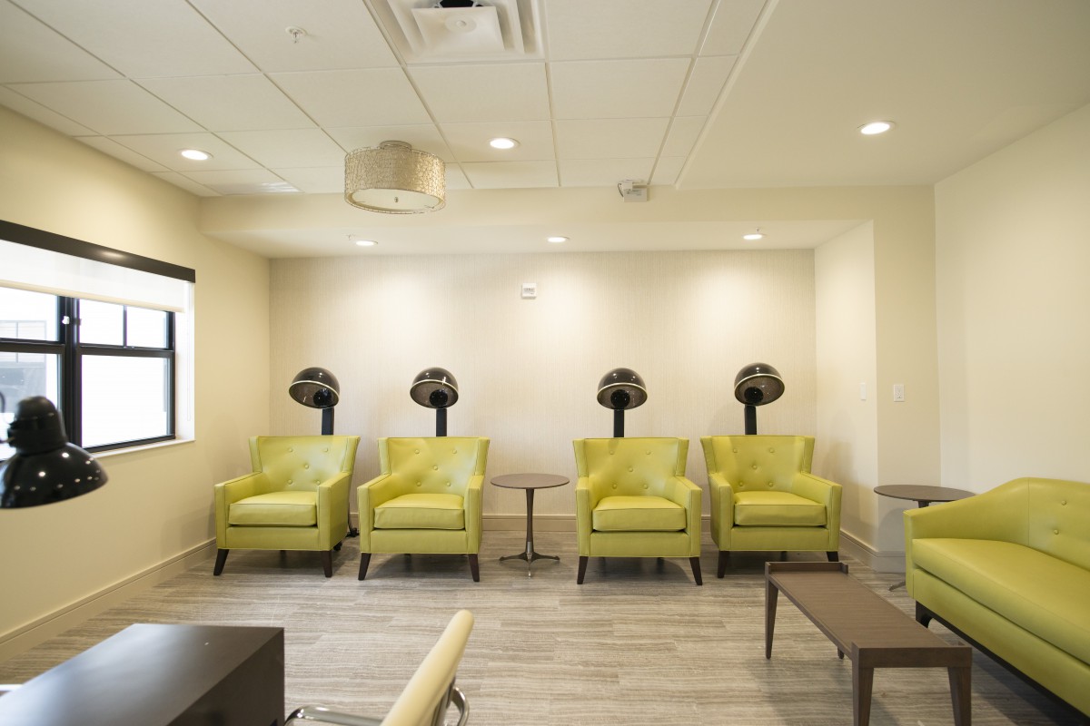 A modern salon waiting area featuring lime green chairs and wall-mounted hair dryers.