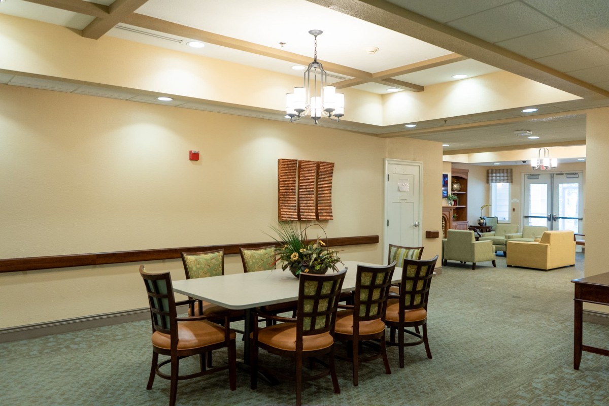 A well-lit dining area featuring a large table surrounded by chairs, with elegant ceiling lights and wall decor.