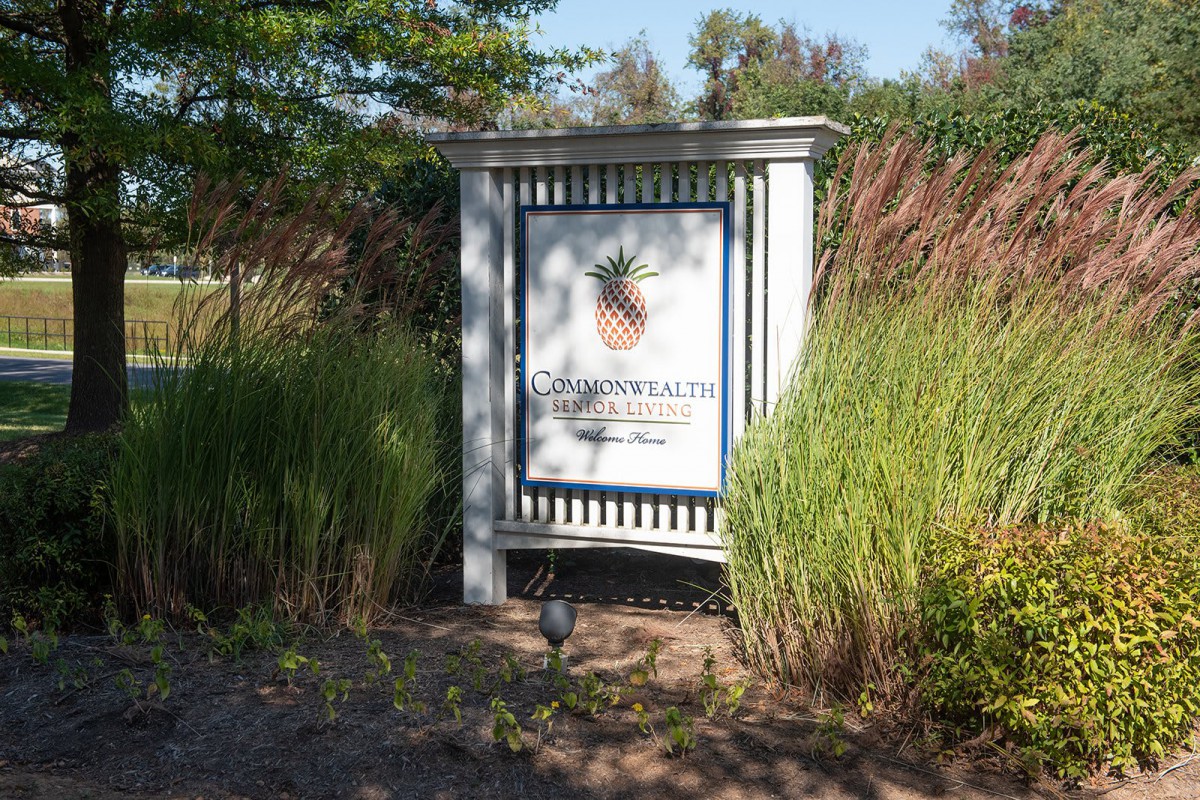 A sign in a garden setting featuring a pineapple design, surrounded by lush greenery.