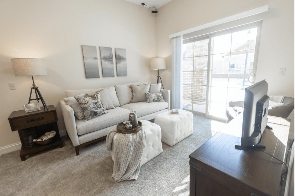 A bright and modern living room with a stylish sofa, coffee table, and decorative accessories, enhanced by natural light from large windows.