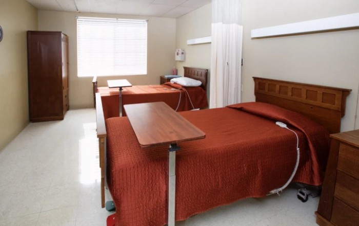 A hospital room with two patient beds, equipped with over-bed tables and medical amenities.