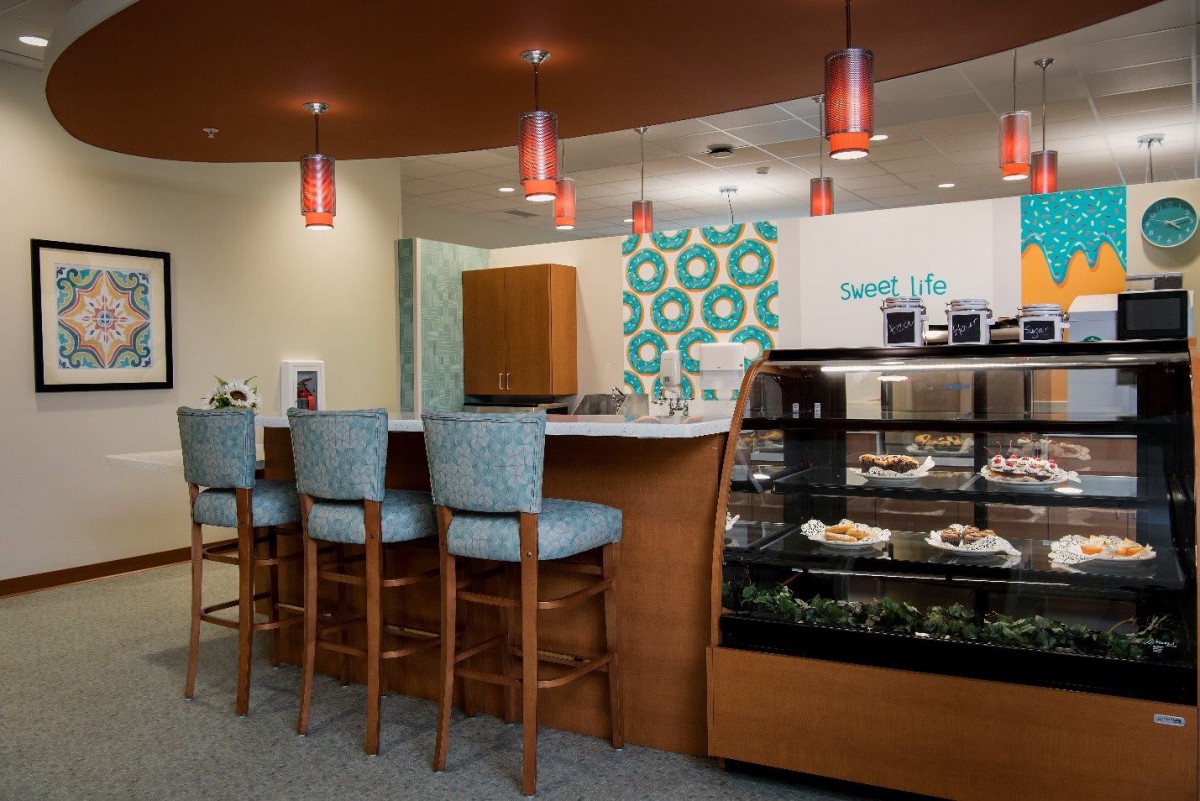 A cozy cafe interior with seating at a counter and a display case filled with treats.
