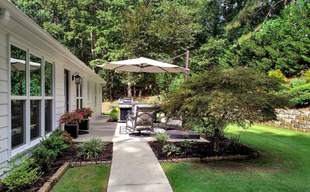 A peaceful backyard patio with outdoor furniture and a large umbrella, surrounded by lush greenery.