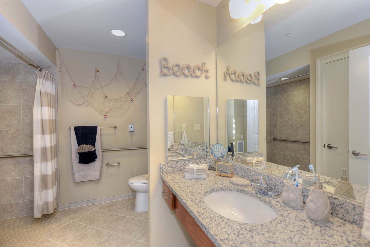 A well-lit bathroom featuring a granite countertop, mirror, and decorative 'Beach House' text on the wall.