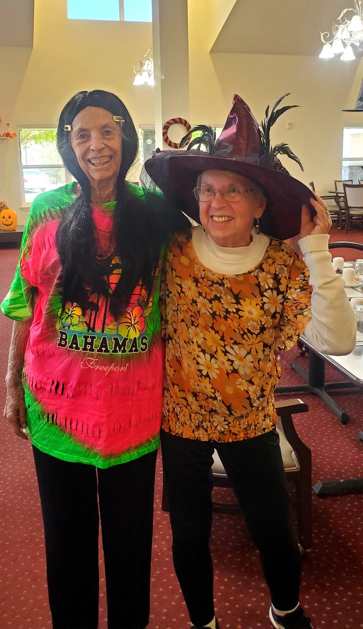Two friends wearing festive costumes and smiling at a Halloween celebration.