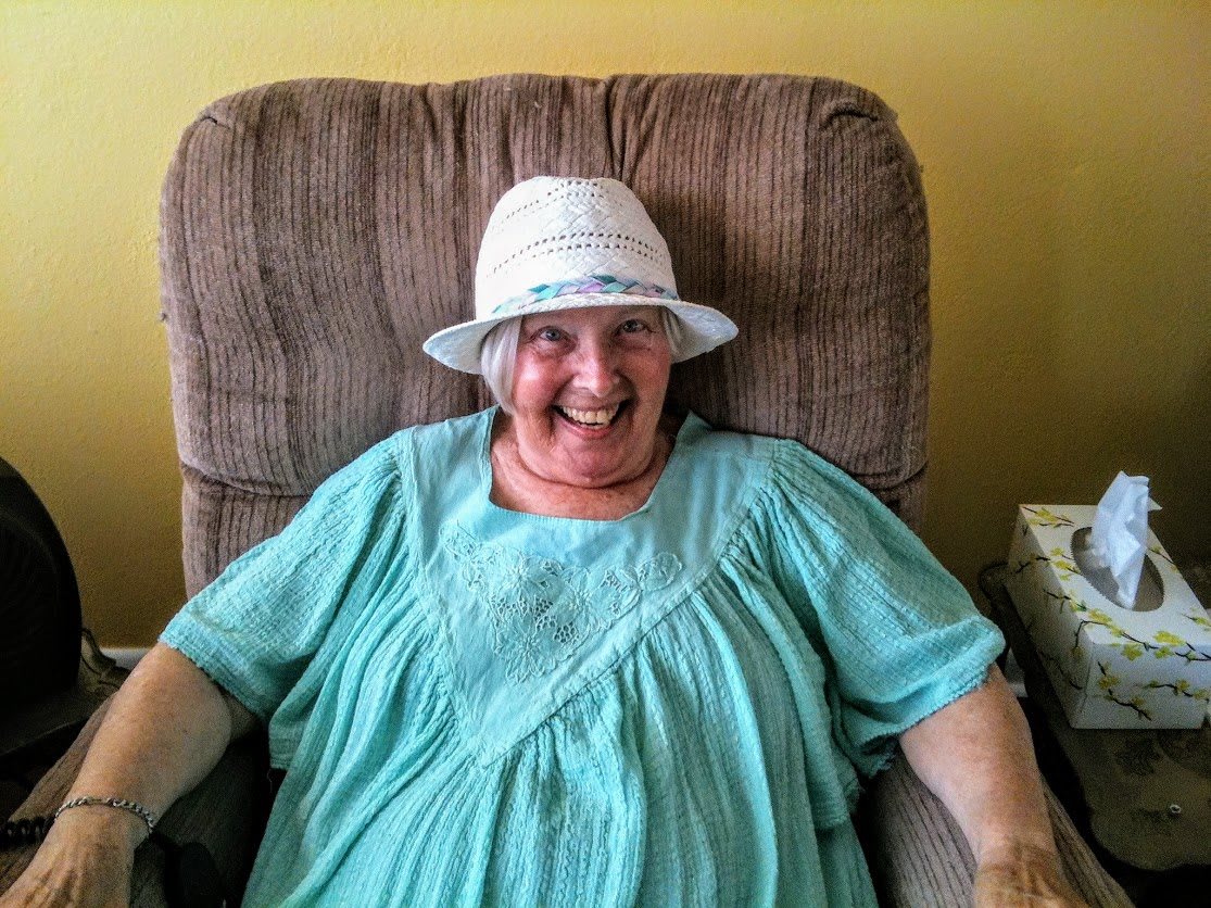 A smiling individual wearing a hat, sitting comfortably in an armchair indoors.