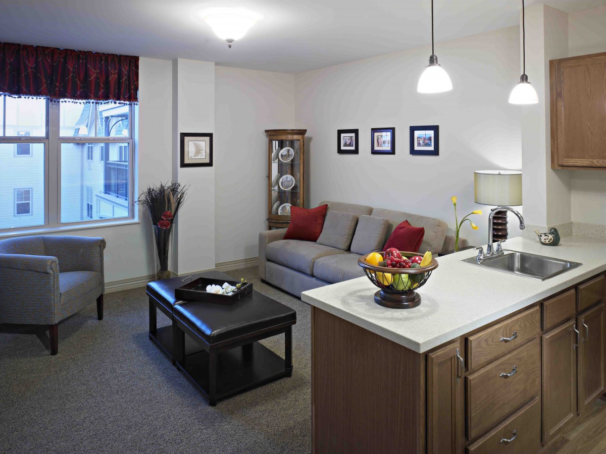 A cozy living room with a comfortable sofa, a coffee table, and a kitchen island adorned with fruit.