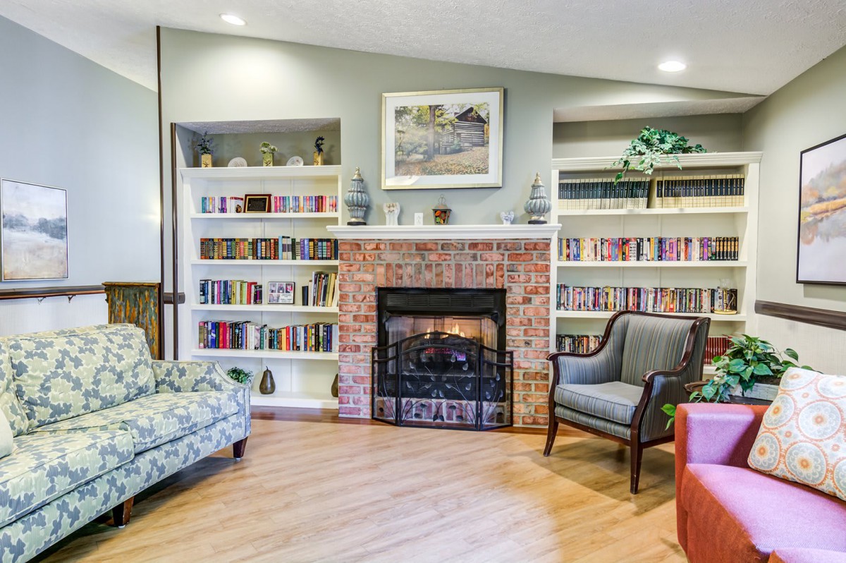 A cozy living room with a brick fireplace, surrounded by bookshelves and comfortable seating.