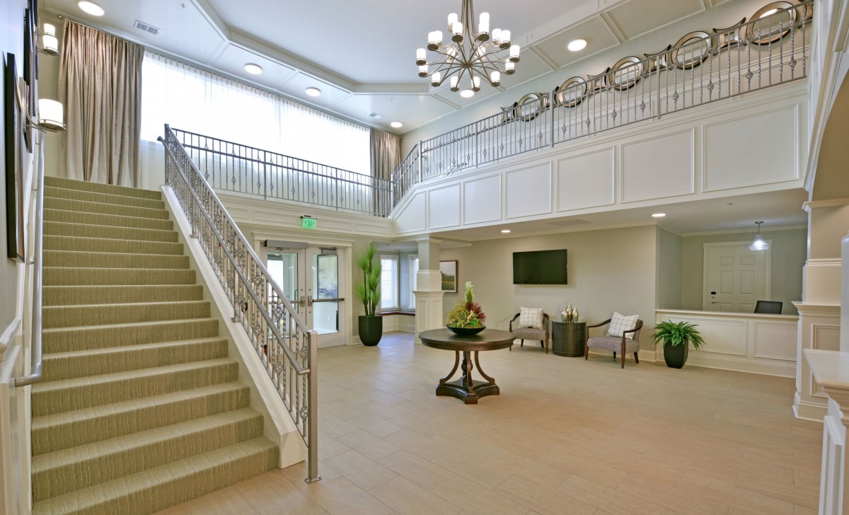 A modern and spacious lobby with a grand staircase, elegant chandelier, and comfortable seating area.