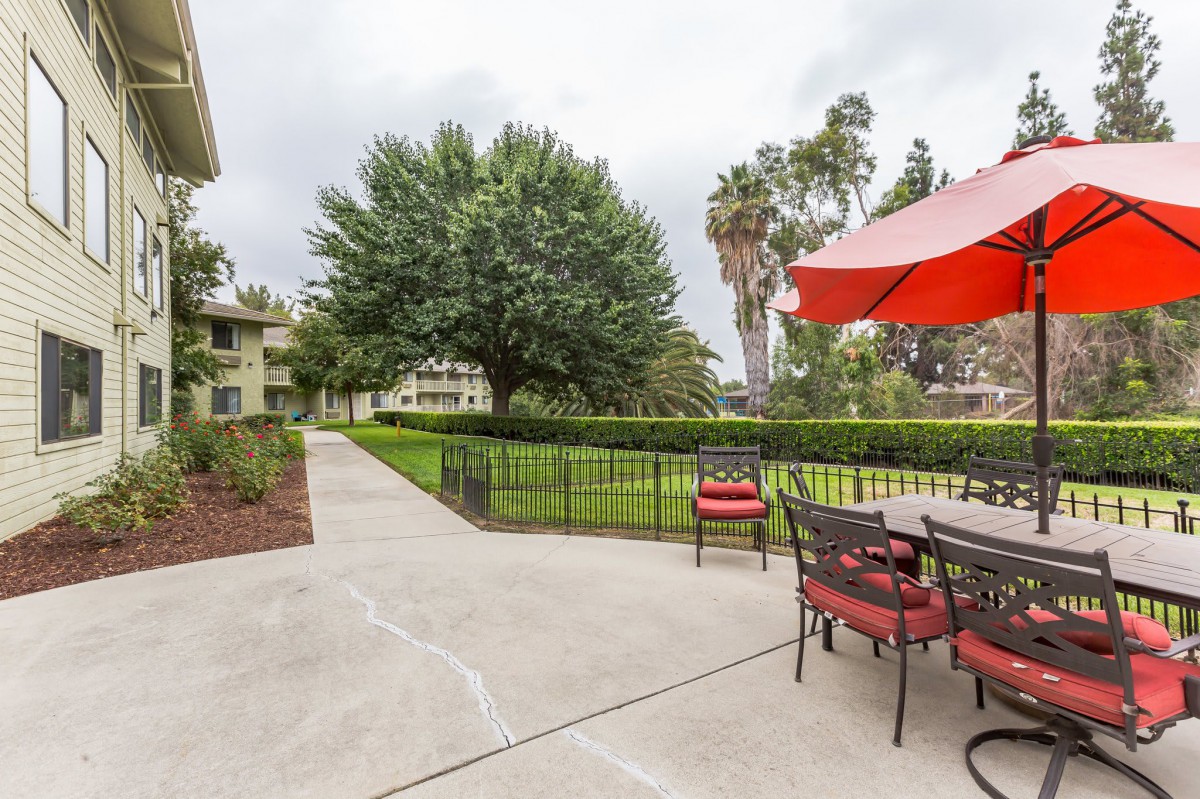 A peaceful outdoor patio area with seating, an umbrella, and a view of a tree-lined landscape.