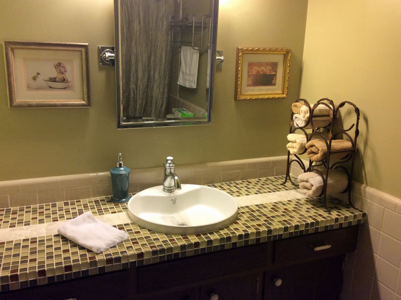 A tidy bathroom with a tiled countertop, featuring a sink, mirror, and neatly arranged towels.