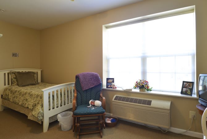 A cozy bedroom with a crib, rocking chair, and large window allowing natural light.