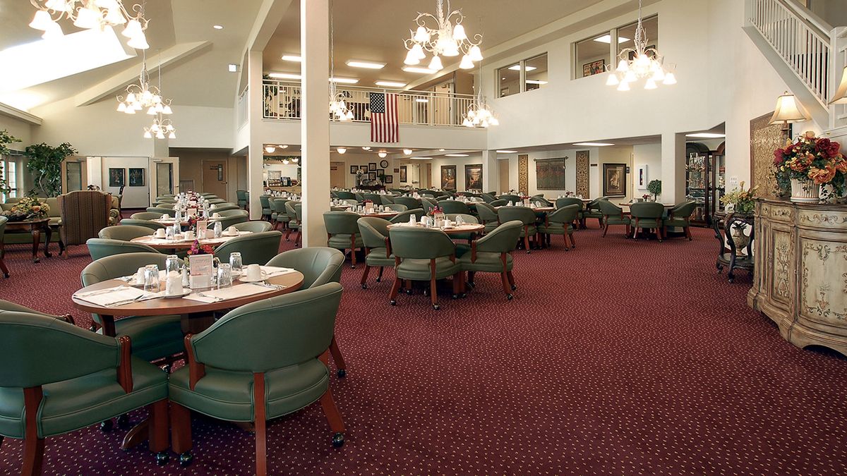 A spacious dining room with neatly arranged tables and chairs, illuminated by elegant chandeliers.