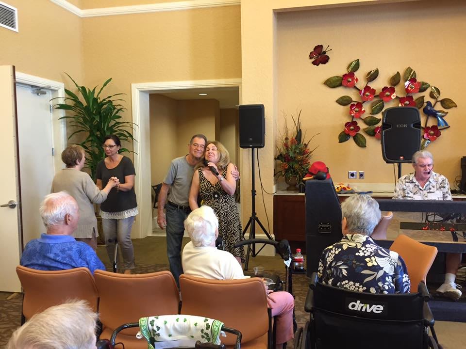 A group of people gathered indoors for an event, with a focus on a woman using a microphone in front of seated attendees.