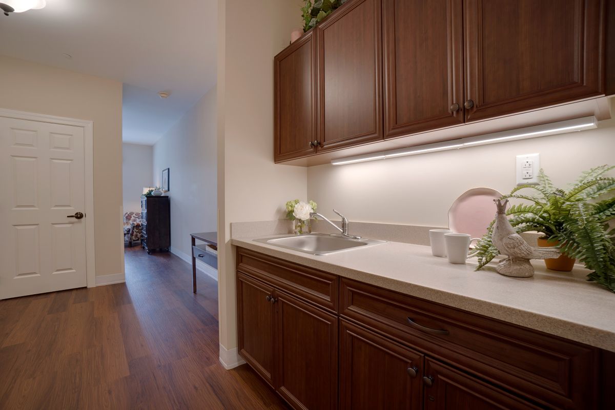 A modern kitchen area with wooden cabinets and a sink, leading into a hallway.